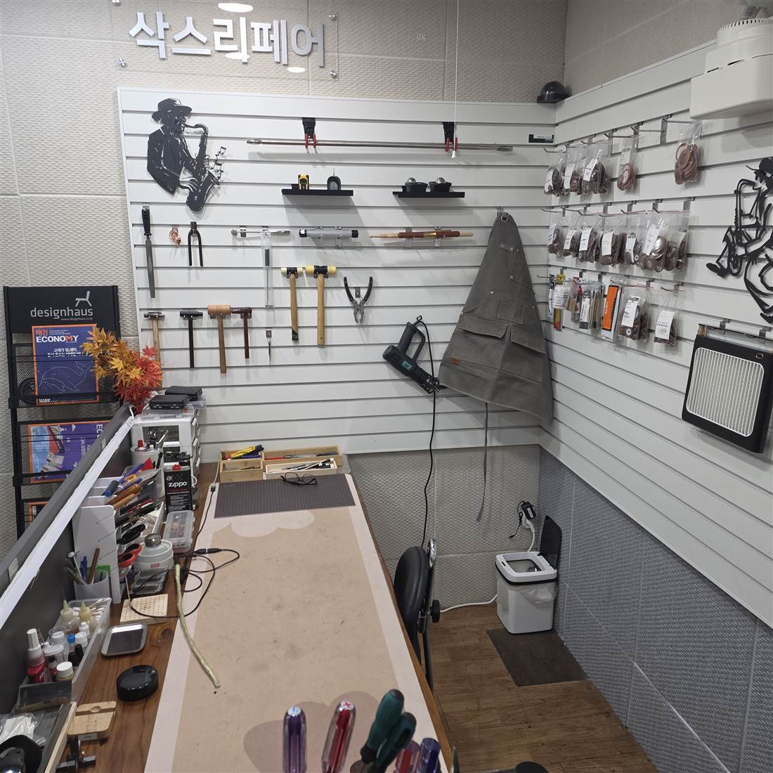 삭스리페어 작업대 — 벽면 슬랫월에 해머·플라이어·히팅건 등 수리 공구와 패드·소모품 봉투가 걸려 있는 모습
